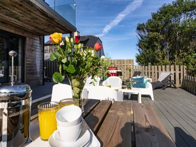 An outdoor patio with a wooden table holding a vase of flowers cups and glasses at Chy Lowen in St Ives