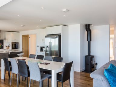 A dining area with a white table and mixed black and gray chairs next to a modern kitchen with stainless steel refrigerator and a black stove with a visible chimney pipe at Boscarne in St Ives