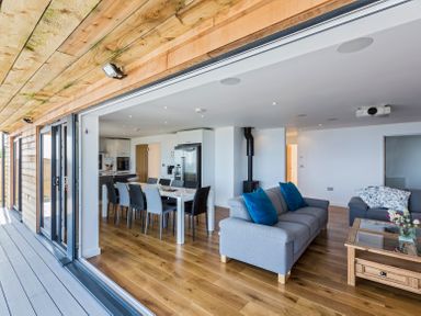 An open living room and kitchen with wooden floors and a dining table with chairs at Boscarne in St Ives