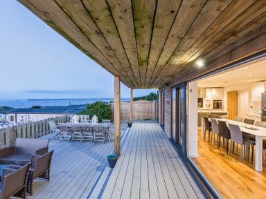 An outdoor wooden deck with dining and seating areas overlooking rooftops and water at Boscarne St Ives