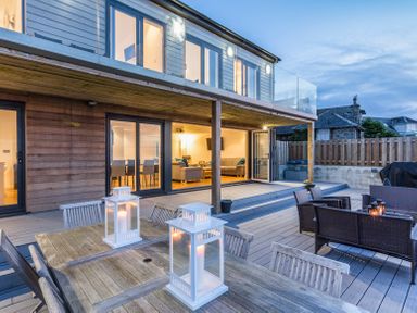 An outdoor deck with wooden dining table and chairs and seating area outside a modern house at Boscarne in St Ives