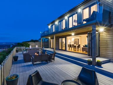 An outdoor deck with chairs, tables, and potted plants overlooking a modern two-story house at Boscarne St Ives