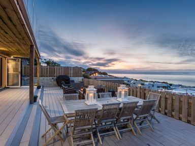 An outdoor wooden deck with a dining table and chairs with lanterns during sunset at Boscarne in St Ives