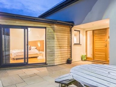 An outdoor patio with wooden round table and a bedroom visible through large glass doors at Boscarne in St Ives