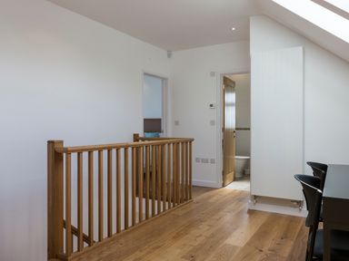 A hallway with wooden railing and wooden floor leading to a bathroom with a wooden door at Boscarne in St Ives