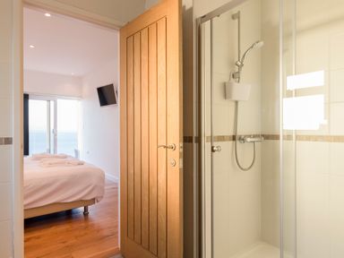 A bathroom with a shower next to a bedroom with a bed and a wall-mounted television at Boscarne in St Ives