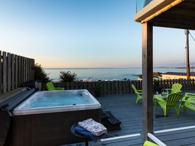 A deck with a hot tub green chairs and tables overlooking the sea at Boscarne in St Ives