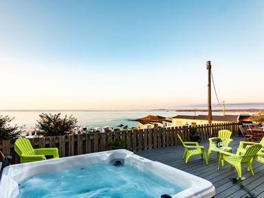 An outdoor deck with a hot tub green chairs a table and a view of the sea at Boscarne in St Ives