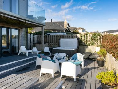 An outdoor patio with white chairs a table a hot tub and potted plants at Boscarne in St Ives