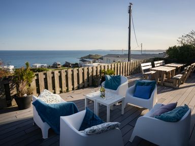An outdoor deck with white chairs and a table overlooking the sea at Boscarne St Ives