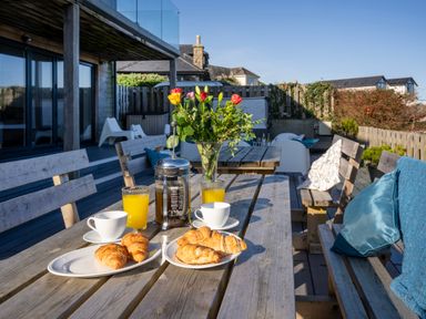 An outdoor patio with wooden tables and benches set with croissants coffee and juice at Boscarne in St Ives