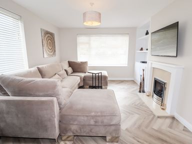 A living room with a beige sectional sofa a fireplace a wall-mounted television and wooden floor at 4 Bodnant Road Rhos-On-Sea