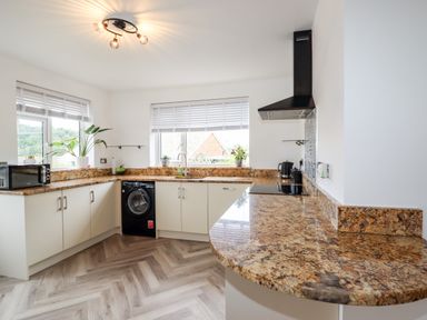 A kitchen with granite countertops a black washing machine a microwave and plants on windowsills at 4 Bodnant Road in Rhos-On-Sea