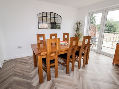 A dining room with a wooden table and six chairs near glass doors and a wall mirror at 4 Bodnant Road in Rhos-On-Sea