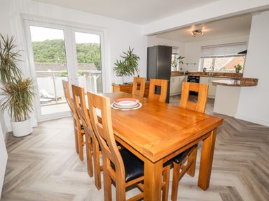 A dining area with a wooden table and chairs near glass doors leading outside and a view of greenery at 4 Bodnant Road in Rhos-On-Sea