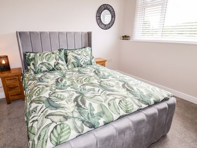 A bedroom with a grey upholstered bed and green leaf patterned bedding at 4 Bodnant Road in Rhos-On-Sea