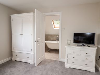 A bedroom with white wardrobe and dresser with a television and door open to bathroom with bathtub at 4 Bodnant Road in Rhos-On-Sea