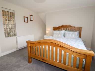 A bedroom with a wooden bed frame a bedside table with a lamp two framed pictures on the wall and a glass block window at 4 Bodnant Road in Rhos-On-Sea