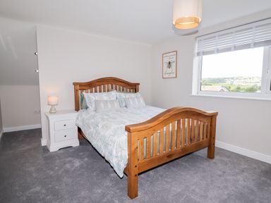 A bedroom with a wooden bed frame white bedside table with lamp and a window showing outdoor view at 4 Bodnant Road in Rhos-On-Sea