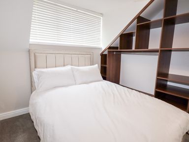 A bedroom with a bed covered in white bedding and a built-in wooden shelving unit at 4 Bodnant Road in Rhos-On-Sea