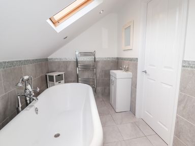 A bathroom with a bathtub sink cabinet towel rack skylight and a white door at 4 Bodnant Road in Rhos On Sea