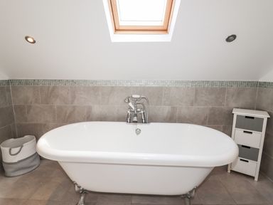 A bathroom with a free standing bathtub a storage basket and a small cabinet at 4 Bodnant Road in Rhos-On-Sea