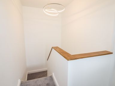 A staircase with a wooden handrail and modern circular ceiling light at 4 Bodnant Road in Rhos-On-Sea
