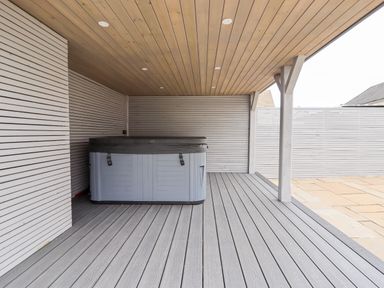 A covered outdoor area with a hot tub on a gray deck at 4 Bodnant Road in Rhos-On-Sea