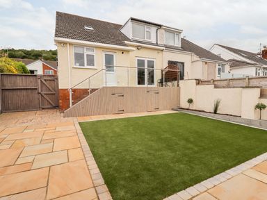 A backyard with artificial grass a patio fence and a two story cream house at 4 Bodnant Road in Rhos-On-Sea