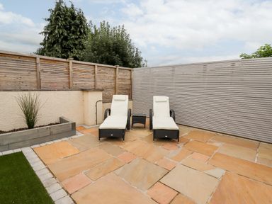 A patio area with two lounge chairs and a small table surrounded by wooden fences at 4 Bodnant Road in Rhos-On-Sea