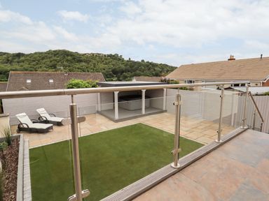 A backyard with artificial grass area tiled patio two lounge chairs and a covered hot tub at 4 Bodnant Road in Rhos-On-Sea