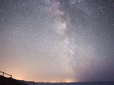 A night sky filled with stars and the milky way over a dark horizon with a fence on the left at The Dovecote in Hartland
