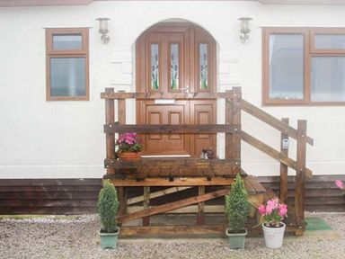 Front entrance of a house with wooden double doors a porch with railings two potted plants on the ground and flowering plants on the porch at The Dovecote in Hartland