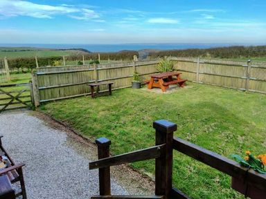 A fenced garden with a picnic table a bench and a gravel path overlooking fields and the sea at The Dovecote in Hartland