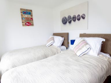 A bedroom with two single beds with striped pillows and beige covers and wall art above the beds at The Dovecote in Hartland