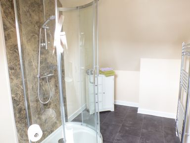 A bathroom with a glass shower enclosure a small white cabinet with folded towels and a heated towel rack at Penylodge in Builth Wells