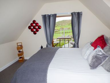 A bedroom with a bed with pillows and a gray blanket a small bookshelf on the floor and a door with gray curtains leading to a balcony at Penylodge in Builth Wells