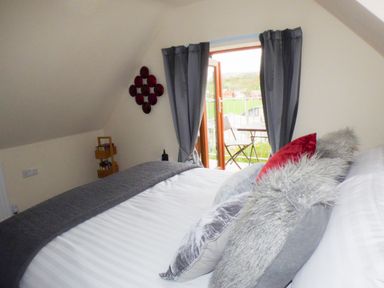 A bedroom with a bed, pillows, a blanket, curtains, an open door, and a balcony at Penylodge in Builth Wells
