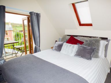 A bedroom with a double bed and multiple cushions next to a balcony with chairs and a table at Penylodge in Builth Wells