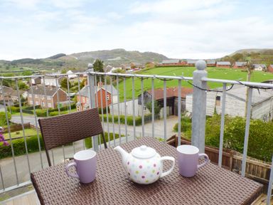 A balcony with a table and two chairs overlooking a rural neighborhood with green fields and hills at Penylodge in Builth Wells