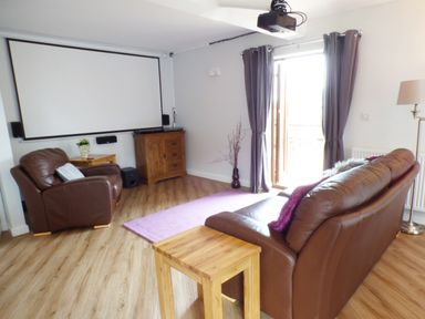 A living room with leather sofa and armchair a projector screen and wooden furniture at Penylodge in Builth Wells