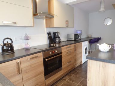 A kitchen with wooden cabinets black countertop kettle microwave coffee maker and washing machine at Penylodge in Builth Wells