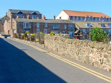 A street with stone houses wooden benches and a low stone wall at Sunnie Cottage in Seahouses