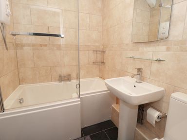 A bathroom with a bathtub shower combination sink toilet and mirror at Sunnie Cottage in Seahouses
