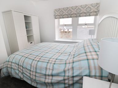 A bedroom with a bed covered in blue and brown plaid bedding a white wardrobe and a window with patterned blinds at Sunnie Cottage in Seahouses
