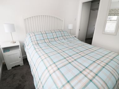 A bedroom with a bed covered by a checkered blanket two nightstands with lamps and a mirror on the wall at Sunnie Cottage in Seahouses