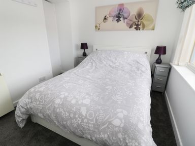 A bedroom with a double bed with patterned bedding purple lamps on bedside tables and flower artwork above the bed at Sunnie Cottage in Seahouses