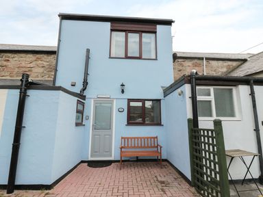 A blue two-story house with a wooden bench outside and a small patio area at Sunnie Cottage in Seahouses