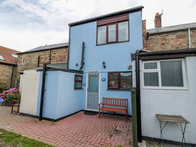 Exterior of a two-story blue cottage with a wooden bench by the front door and a small table nearby at Sunnie Cottage in Seahouses