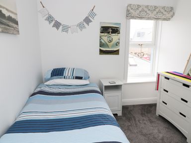 A bedroom with a single bed with striped bedding a nightstand a window and a chest of drawers at Sunnie Cottage in Seahouses